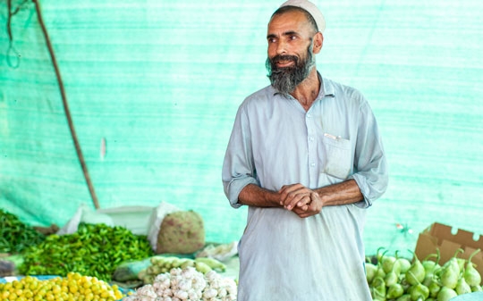 A man selling vegetables in Pakistan behind a green background