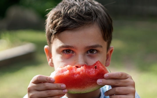 Child holding a piece of watermelon in front of his eyes