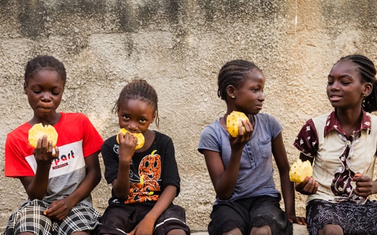 Kids in Nigeria sitting down on a bench and eating yellow fruit