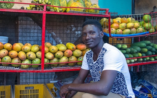 Man sitting in front of mangoes, papayas and other fruits in Tanzania