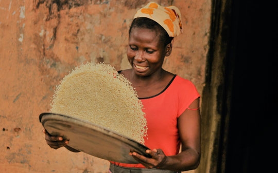 Woman smiling warmly while shaking a basket with rice in Nigeria