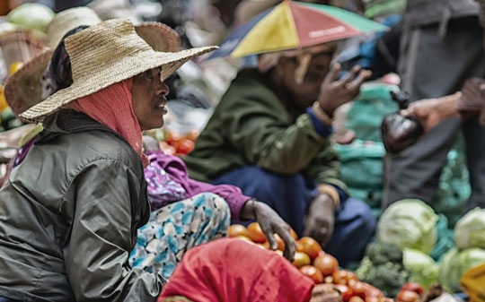 Woman wearing a hat and jacket sitting on the ground of a market in Ethiopia