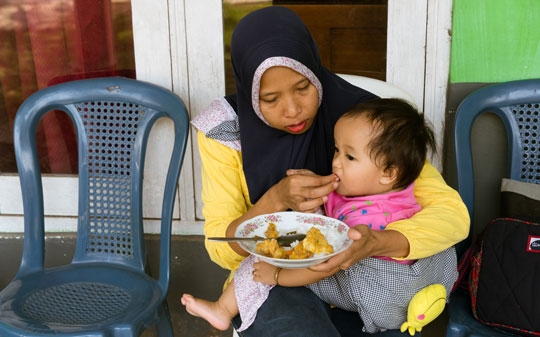 A mother in Indonesia giving her child food from her lap