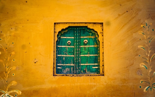 Green window shutters against yellow wall