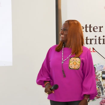 Joyce wearing a pink blouse and smiling towards the screen