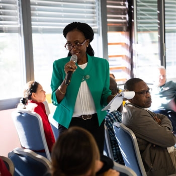 Prisca standing up and talking in the microphone in a room filled with people